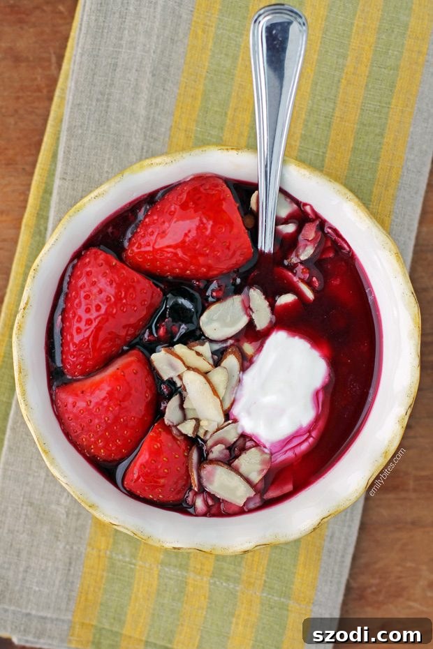 A vibrant Triple Berry Yogurt Bowl with warm berries, Greek yogurt, honey, sliced strawberries, and almonds