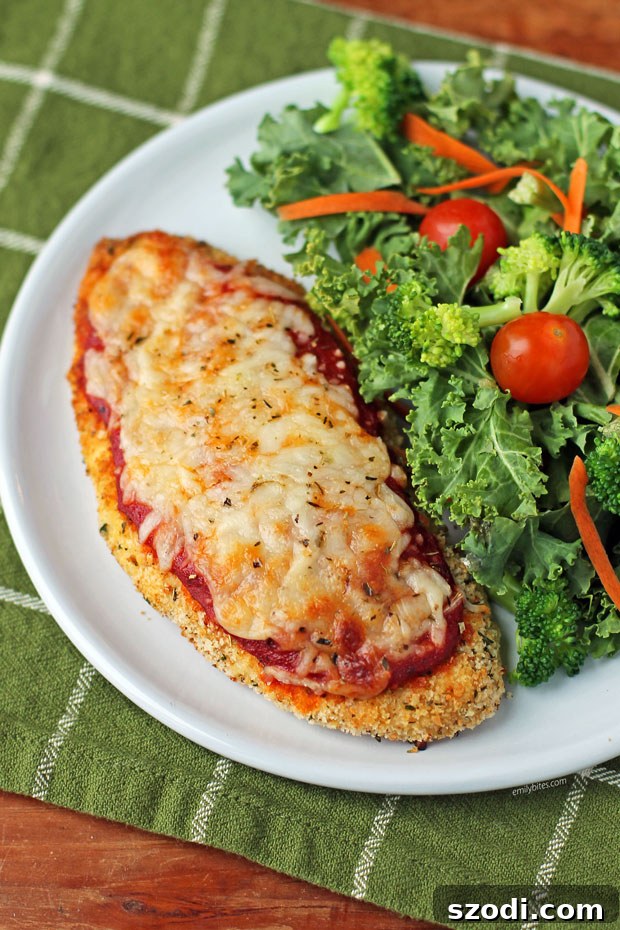 Plate of Lighter Crispy Chicken Parmesan served with a vibrant fresh side salad, creating a balanced meal.