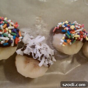 Frozen Chocolate Banana Bites, half-dipped in chocolate and coated with colorful sprinkles and shredded coconut on a tray.