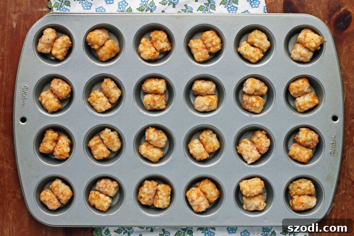 Frozen tater tots arranged in a mini muffin tin, ready for baking into cups.