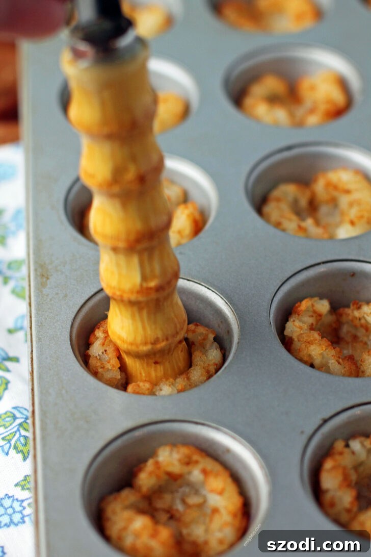 A kitchen utensil pressing down on baked tater tots in a muffin tin to form perfect cups.