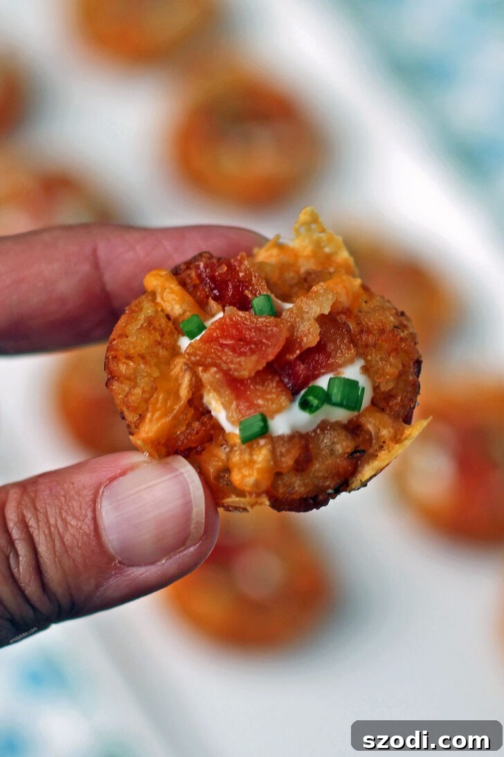 A hand holding a single Mini Loaded Tater Tot Cup, showcasing its perfect bite-sized form and delicious toppings.